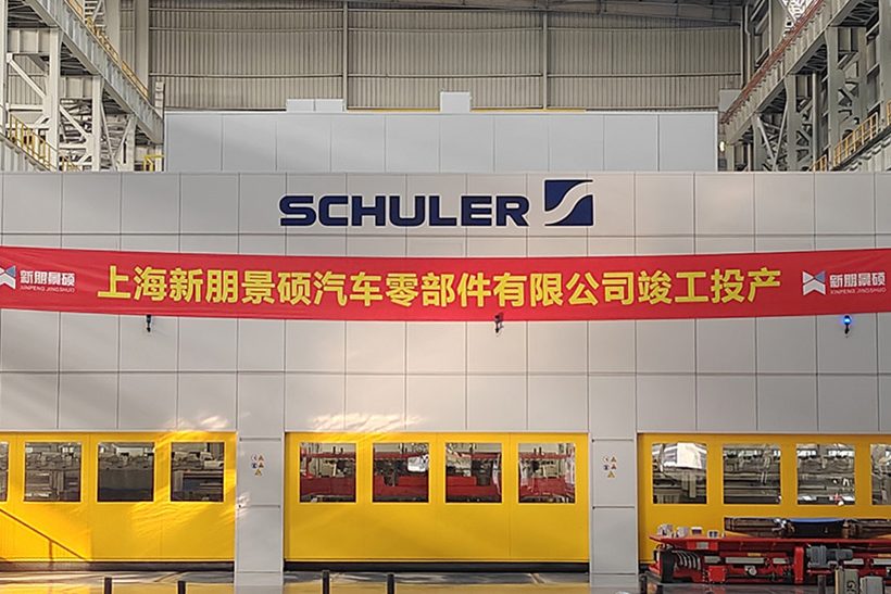 Das Bild zeigt eine Werkshalle des chinesischen Unternehmens Xin Peng. An einer Wand hängt ein rotes banner mit chinesischen Schriftzeichen, darunter sind drei gelbe Maschinen zu sehen.