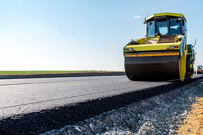 Das Bil zeigt am rechten Bildrand eine gelbe Walze, die eine frisch geteerte Straße walzt. Im Straßenbau werden Gesteinskörnungen aus Eisenhüttenschlacke seit Jahrzehnten im eingesetzt.