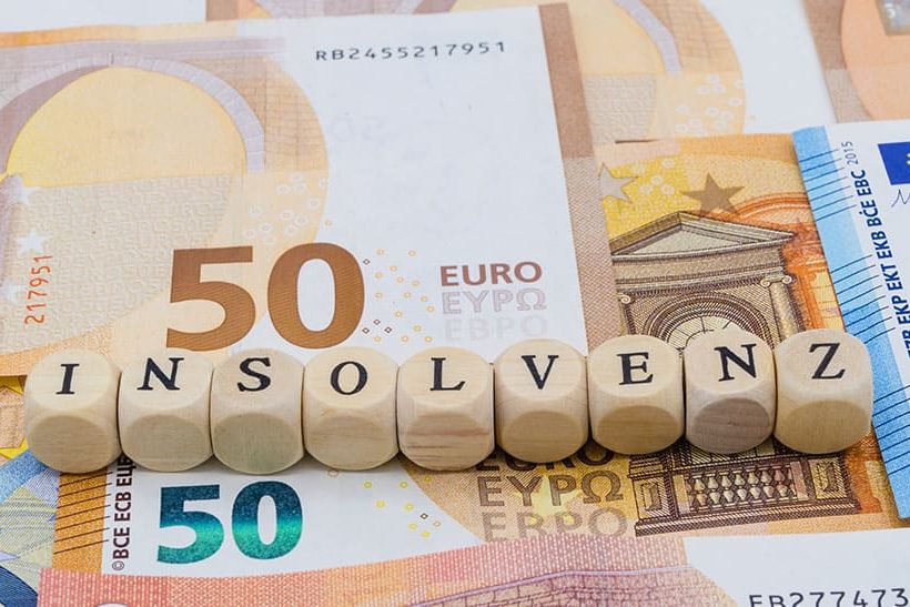 Das Bild zeigt neun Würfel, die nebeneinander liegen und das Wort Insolvenz bilden. Unter den Würfeln liegen Geldscheine. In dem dazugehörigen Artikel geht es um die Insolvenzantragspflicht.