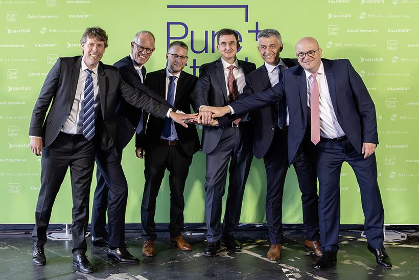 Das Bild zweigt sechs weiße Männer mittleren Alters in Anzügen, die vor einer grünen Wand stehen. Es handelt sich dabei um den neuen Vorstand der SHS – Stahl-Holding-Saar.