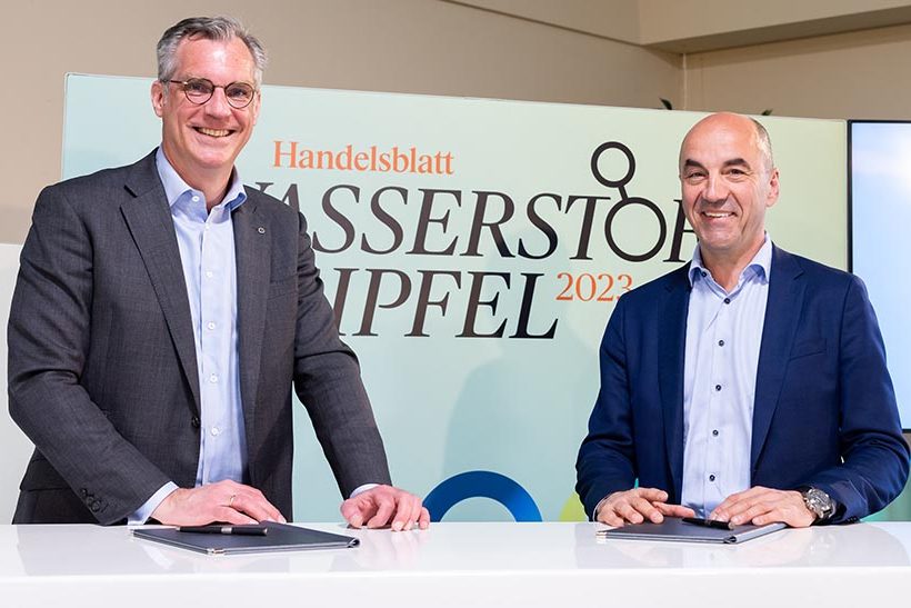 Das Bild zeigt zwei Männer mittleren Alters ab der Hüfte aufwärts, die Sakkos tragen und an einem Tisch stehen. Es sind Gunnar Groebler (Salzgitter AG, links) und Stefan Dohler (EWE). Die beiden lächeln in Richtung des Betrachters, da sie gerade eine Kooperationsvereinbarung für Wasserstoff abgeschlossen haben.