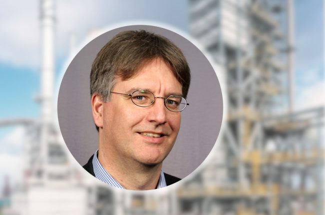 Das Bild zeigt eine Collage: Im Vordergrund ist der Kopf eines weißen Mannes als kreisrunder Ausschnitt zu sehen, im Hintergrund und unscharf die Circored-Anlage in Trinidad.