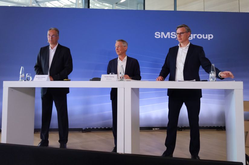 Das Bild zeigt drei Führungskräfte der SMS group bei einer Pressekonferenz.