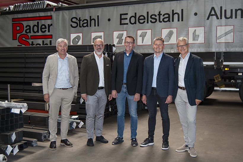 Fünf Männer stehen in einer Lagerhalle, Im Hintergrund ist ein LKW mit dem Schriftzug Pader-Stahl.