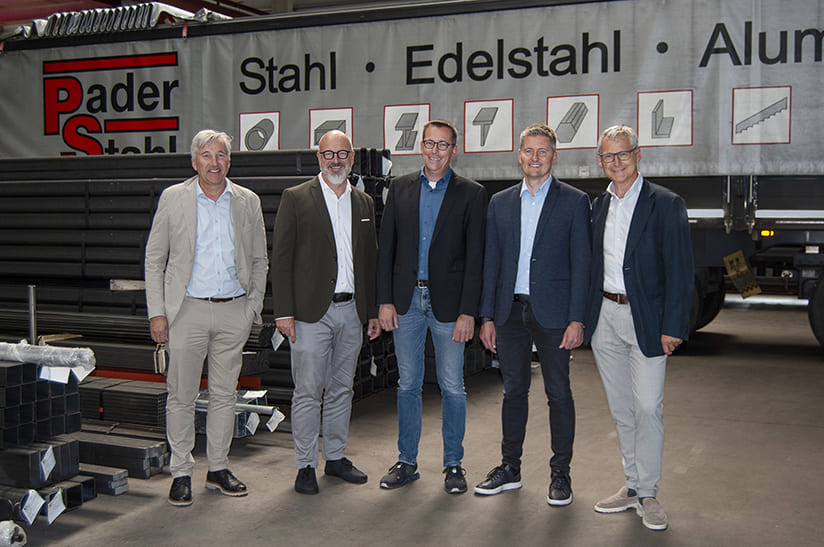 Pader-Stahl (small) Fünf Männer stehen in einer Lagerhalle, Im Hintergrund ist ein LKW mit dem Schriftzug Pader-Stahl.