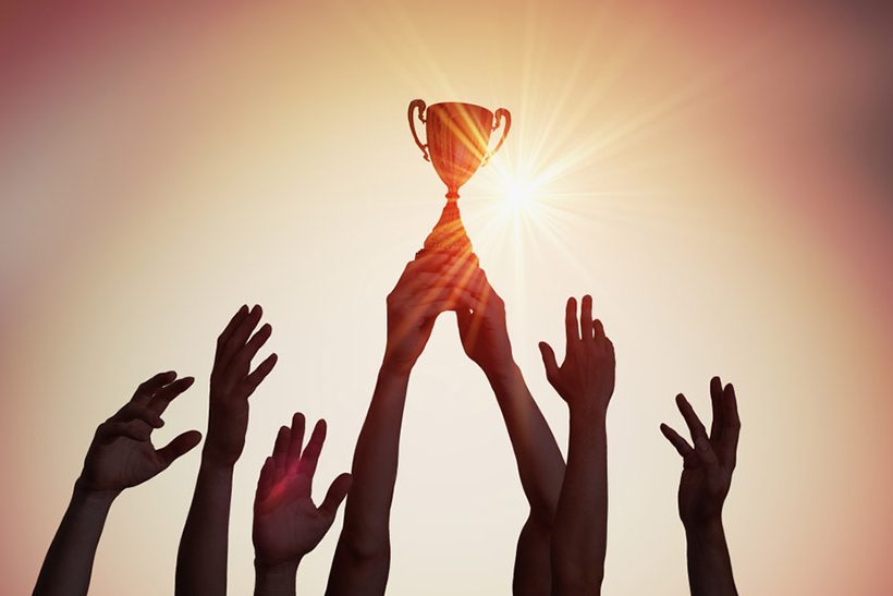 Das bild zeigt im Gegenlicht sieben in die Höhe gereckte Unterarme. Ein paar Hände hält dabei einen Pokal fest. Das Bild steht sinnbildlich für die jüngste Auszeichnung von Dillinger.