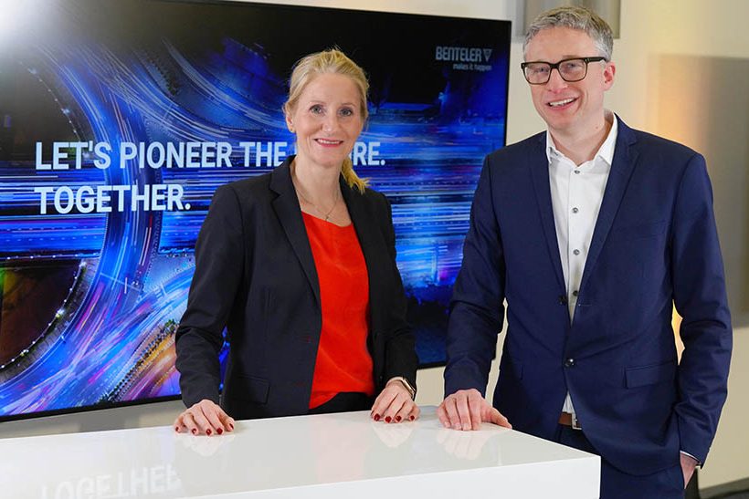 Das Bild zeigt eine weiße Frau (Birgit Held) und einen weißen Mann (Stephan Knüttel), die an einem Stehtisch stehen. Sie tragen Business-Kleidung und gehören zum Unternehmen Benteler.