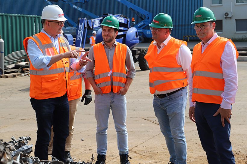 Das Bild zeigt vier Männer in Sicherheitskleidung auf dem Gelände der TSR40-Anlage in Duisburg. Einer trägt einen weißen Helm (links), die anderen jeweils einen grünen Helm.