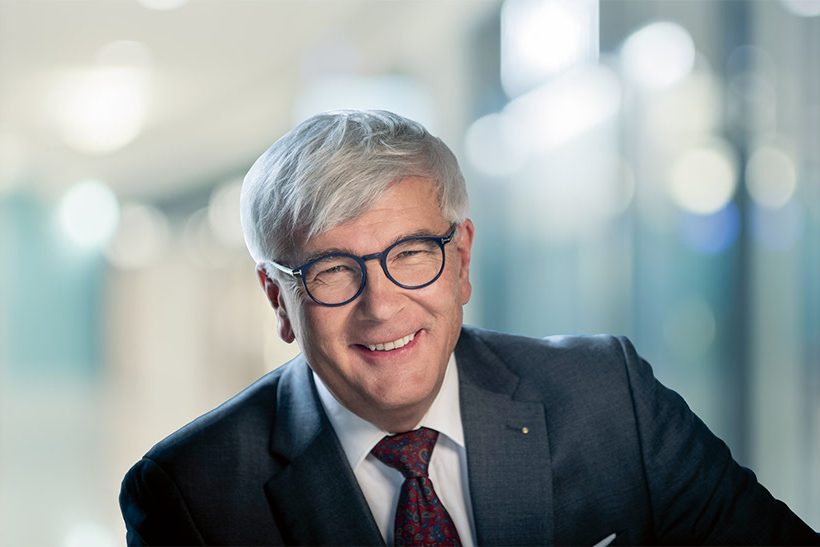 Das Bild zeigt das Porträt eines weißen, grauhaarigen Mannes. Er trägt eine Brille, einen Anzug mit Krawatte und lächelt in die Kamera. Es handelt sich dabei um Reinhard Noebauer von Voestalpine.