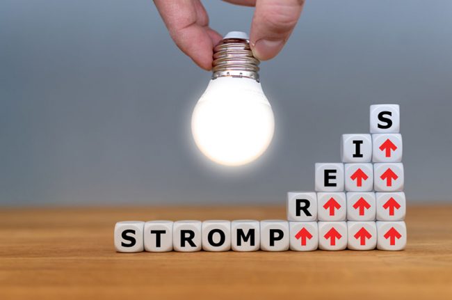 Symbol,For,Increasing,Electricity,Rates.,Dice,Form,The,German,Word Das Bild zeigt Würfel mit Buchstaben und roten Pfeilen, die für den steigenden Strompreis stehen. Eine helle Glühbirne soll die Idee der Siempelkamp Giesserei andeuten, wie das Problem gelöst werden kann.