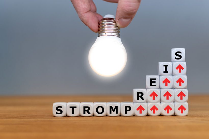 Das Bild zeigt Würfel mit Buchstaben und roten Pfeilen, die für den steigenden Strompreis stehen. Eine helle Glühbirne soll die Idee der Siempelkamp Giesserei andeuten, wie das Problem gelöst werden kann.