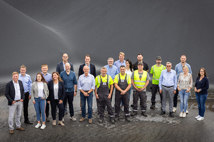 Erzkontor_HAG (web) Das Bild zeigt eine Gruppe von 21 Menschen in Büro- und Arbeitskleidung. Es handelt sich um Mitarbeiter von Cremer Erzkontor und HAG.