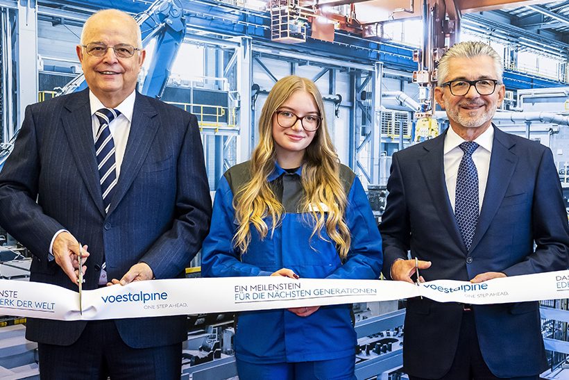 Das Bild zeigt männliche Anzugträger (Führungskräfte) und in ihrer Mitte eine junge Frau im sogenannten Blaumann (Arbeiterin). Alle drei gehören zu Voestalpine und schneiden symbolisch ein Band anlässlich einer Eröffnungsfeier in Kapfenberg durch.