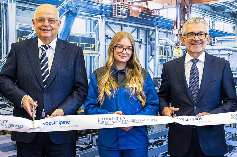2023-10-18-Erîffnung Edelstahlwerk Kapfenberg (web) Das Bild zeigt männliche Anzugträger (Führungskräfte) und in ihrer Mitte eine junge Frau im sogenannten Blaumann (Arbeiterin). Alle drei gehören zu Voestalpine und schneiden symbolisch ein Band anlässlich einer Eröffnungsfeier in Kapfenberg durch.