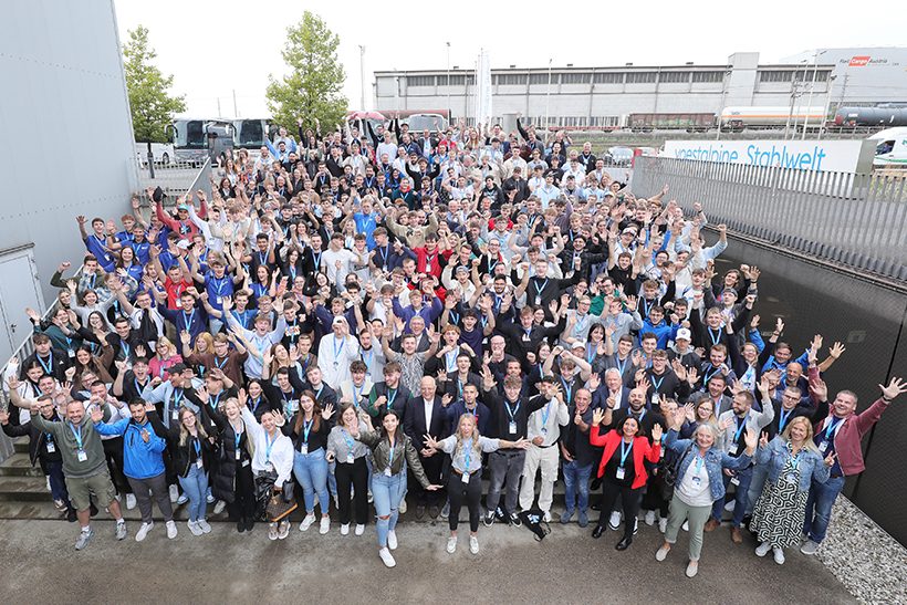 Das Bild zeigt eine große Gruppe junger Menschen, Azubis von Voestalpine im letzten Ausbildungsjahr, die in die Kamera grüßen und lachen.