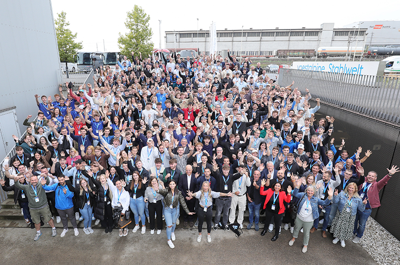 Konzernlehrlingstag-2023_075 (web) Das Bild zeigt eine große Gruppe junger Menschen, Azubis von Voestalpine im letzten Ausbildungsjahr, die in die Kamera grüßen und lachen.