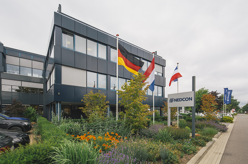 NEDCON – Doetinchem web Das Unternehmen zeigt ein Bürogebäude, vor dem Länderflaggen wehen. Es handelt sich dabei um den Sitz von Nedcon, einem Unternehmen von Voestalpine.