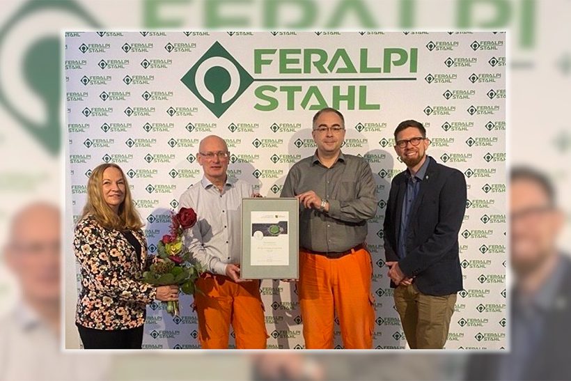 Das Bild zeigt vier Menschen, von denen zwei eine Urkunde halten. Diese geht an Feralpi Stahl für die Mitgliedschaft in der Klima- und Umweltallianz Sachsen.