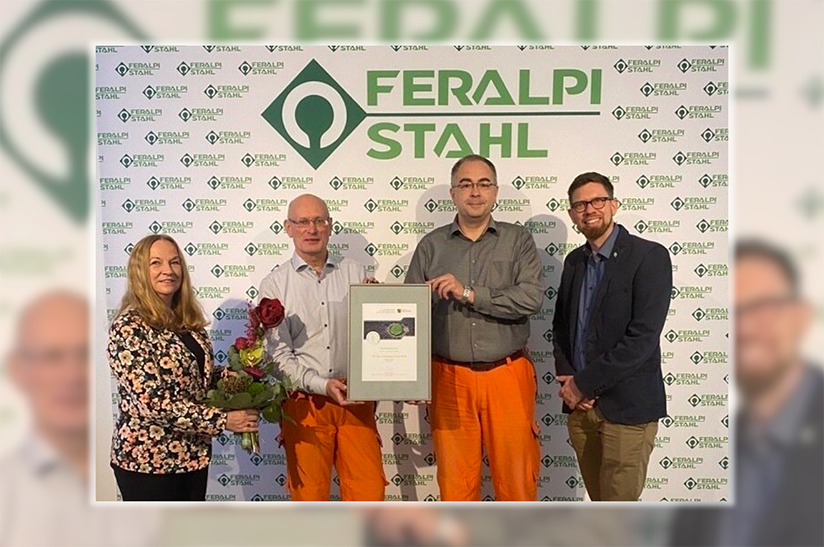 Das Bild zeigt vier Menschen, von denen zwei eine Urkunde halten. Diese geht an Feralpi Stahl für die Mitgliedschaft in der Klima- und Umweltallianz Sachsen.