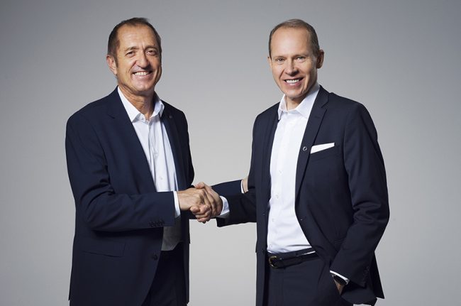 Das Foto zeigt zwei weiße, anzugtragende Männer, die sich die Hand schütteln. Es sind die Führungsköpfe von Outokumpu und Cronimet.