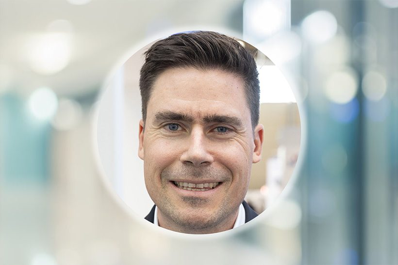 Das Bild zeigt das kreisrund ausgeschnitte Porträt eines weißen Mannes mittleren Alters. Es handelt sich um Simon Scherrenbacher von der Schuler Group. Der Hintergrund ist unscharf.