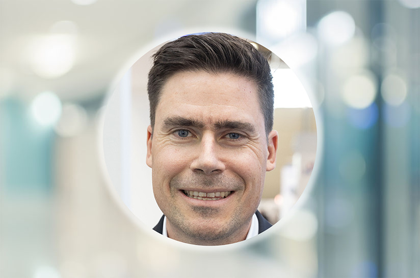 Das Bild zeigt das kreisrund ausgeschnitte Porträt eines weißen Mannes mittleren Alters. Es handelt sich um Simon Scherrenbacher von der Schuler Group. Der Hintergrund ist unscharf.