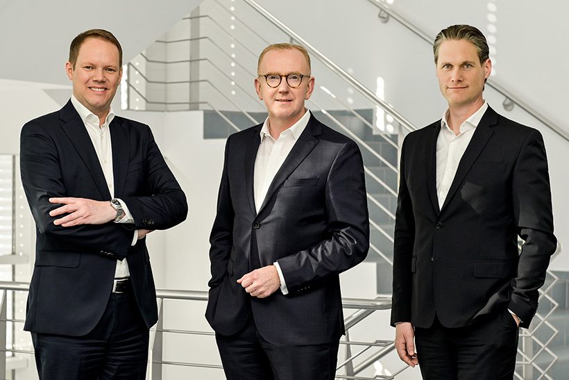 Das Bild zeigt drei weiße Männer in dunklen Anzügen. Sie stehen in einem Trepenhaus. Es sind die Führungskräfte von Technotrans.