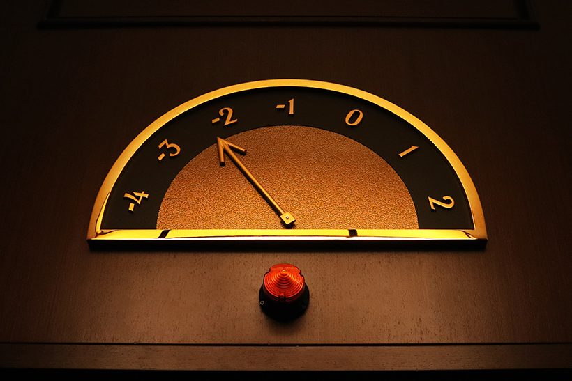 Die stahlproduktion-arcelormittal-blechexpo-2021 2023 in Deutschland sank deutlich. Dem Trend entsprechend zeigt das Bild die Anzeige der Etagennummer eines Aufzugs auf hölzerner Textur. Der Zeiger ist golden und die Zahlen sind altmodisch.