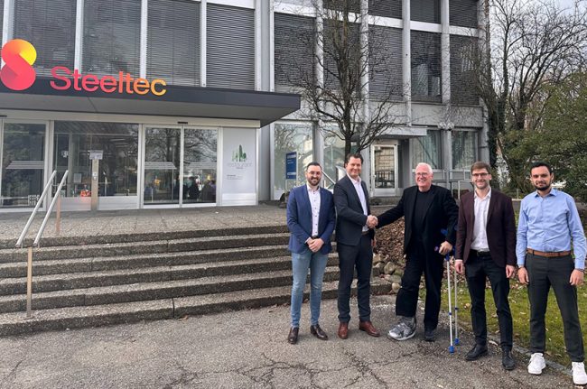 Die Swiss Steel Group setzt die Viridis Energy and Sustainability Suite von der SMS group ein. Das Bild zeigt fünf Männer aus beiden Unternehmen, die vor einem Gebäude einer Unternehmenstochter von Swiss Steel stehen.