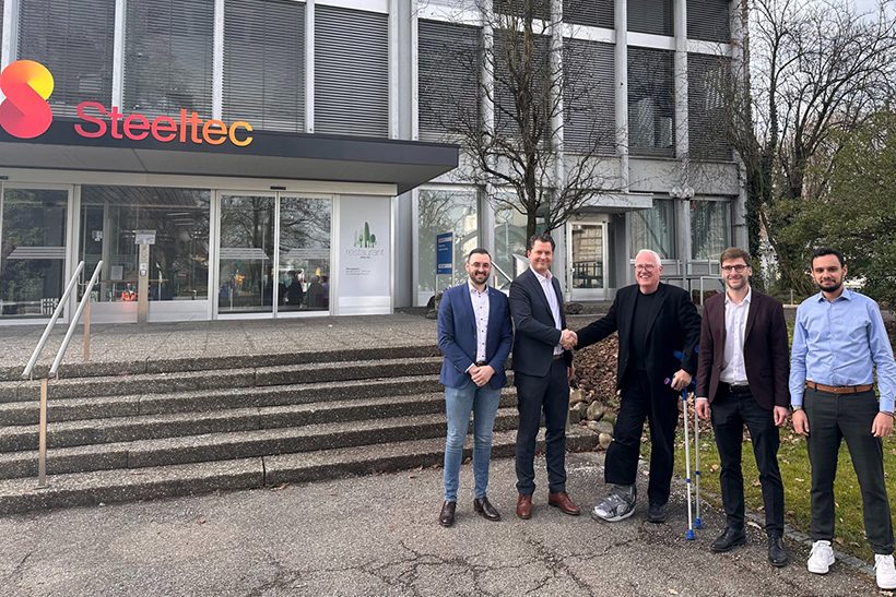 Die Swiss Steel Group setzt die Viridis Energy and Sustainability Suite von der SMS group ein. Das Bild zeigt fünf Männer aus beiden Unternehmen, die vor einem Gebäude einer Unternehmenstochter von Swiss Steel stehen.