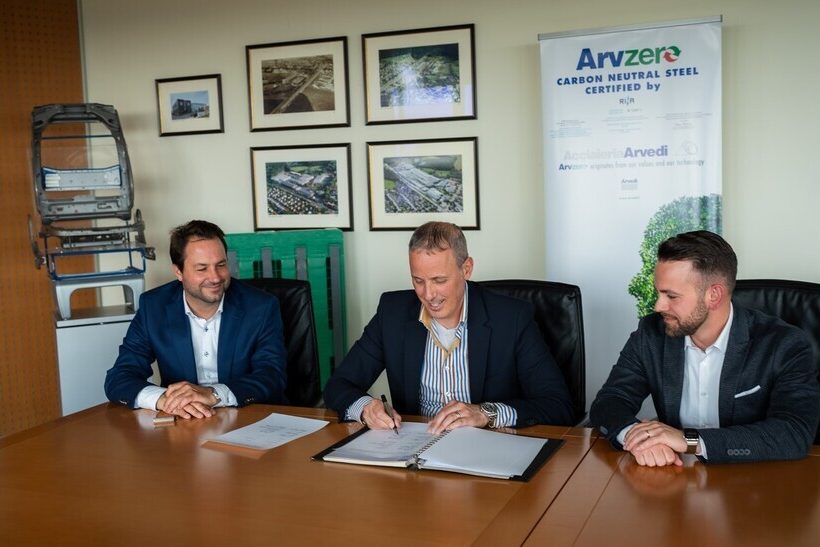 Das Bild zeigt drei Männer an einem Konferenztisch. Der Mann in der Mitte unterzeichnet einen Vertrag. Im Hintergrund ist ein Rollup-Display zum Produkt Arvzero zu sehen.