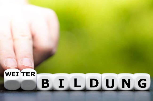 Das Bild zeigt eine Reihe von Würfeln mit Buchstaben und zwei Finger, die zwei Würfel umdrehen. Der Hintergrund ist grün, was zum Projekt GreenSteelSkills passt, das Kompetenzen für die grüne Stahlerzeugung vermitteln will.