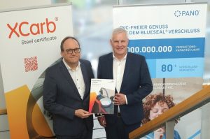 Das Bild zeigt zwei Männer, die ine inem Treppenhaus stehen und ein Din-A4-großes Dokument hochhalten. Es handelt sich dabei um Reiner Blaschek (links) und Thomas Stock. Die beiden dokumentieren die Partnerschaft zwischen ArcelorMittal und Pano.