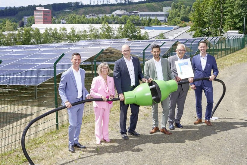 Das Bild zeigt Führungskräfte von Schäfer Werke, die einen überdimensionierten grünen Stromstecker halten. Beim Aufbau der Solaranlage im Hintergrund kam CO2-reduzierter Stahl von ArcelorMittal zum Einsatz.