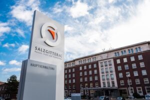 Das Foto zeigt eine Stele mit dem Unternehmenslogo der Salzgitter AG. Im Hintergrund ist ein Firmengebäude zu sehen. Das Salzgitter-Konzern Halbjahresergebnis 2025 weist ein positives EBITDA auf.