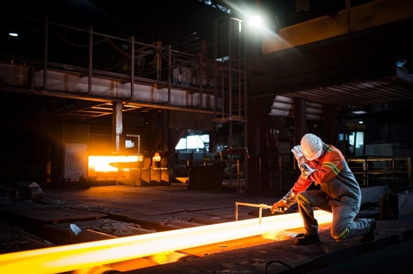 Das Bild zeigt eine Szene aus einem Walzwerk: Ein Mitarbeiter von Buderus Edelstahl kniet neben einem glühenden Block.