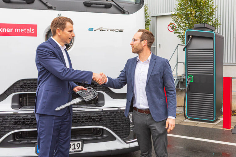 Pressefoto_002_Kloeckner CEO Felix Schmitz_links_Johannes Franz_rechts_Leiter Nutzfahrzeugzentrum, Daimler Truck AG Nutzfahrzeugzentrum Mercedes-Benz Würzburg_web Felix Schmitz, CEO von Kloeckner Metals Germany (li.) erhält von Johannes Franz (Leiter Nutzfahrzeugzentrum Daimler Truck AG, re.) einen überdimensionalen Schlüssel. Die beiden stehen vor einem eActros 600.